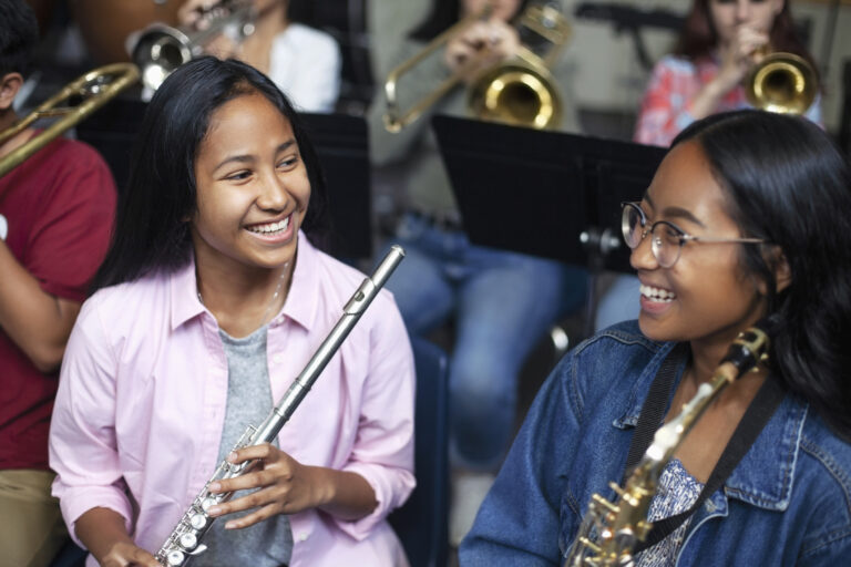 Asian mixed race teenage female music students talking and laughing with brass instruments in class stock photo